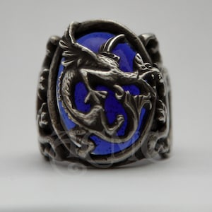 May include: A silver ring with a blue glass stone featuring a detailed dragon design.