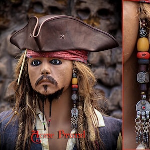 May include: A brown leather pirate hat with a red bandana, and long beaded earrings. The person in the image has long, wavy, blonde hair and a goatee. The image has the text "Home Brand" in red.