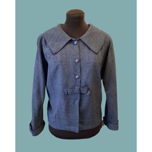 以下が含まれることがあります： 大きな襟、長袖、リボンディテールが特徴のグレーのヴィンテージジャケット。 ジャケットは前面に3つのボタンがあり、マネキンに展示されています。 生地は微妙な斑点のある質感です。