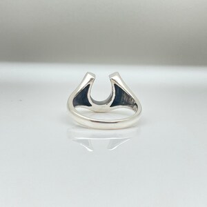 May include: A silver ring with a horseshoe design. The horseshoe is open at the top and the ring is polished.
