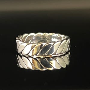 Puede incluir: Un anillo de plata con un diseño trenzado. El anillo es grueso y tiene una forma redondeada.