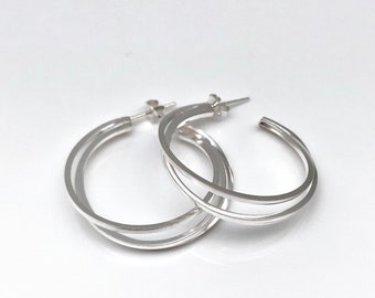 May include: Silver hoop earrings with a double-layered design. The earrings are simple and elegant.