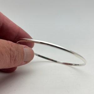 Pode incluir: Um bracelete de prata com acabamento liso e polido. O bracelete é aberto e tem uma ligeira curvatura.
