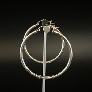 May include: A pair of silver hoop earrings on a display stand. The earrings are simple and elegant.
