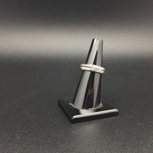 May include: A silver ring with a textured design. The ring is displayed on a black ring stand.