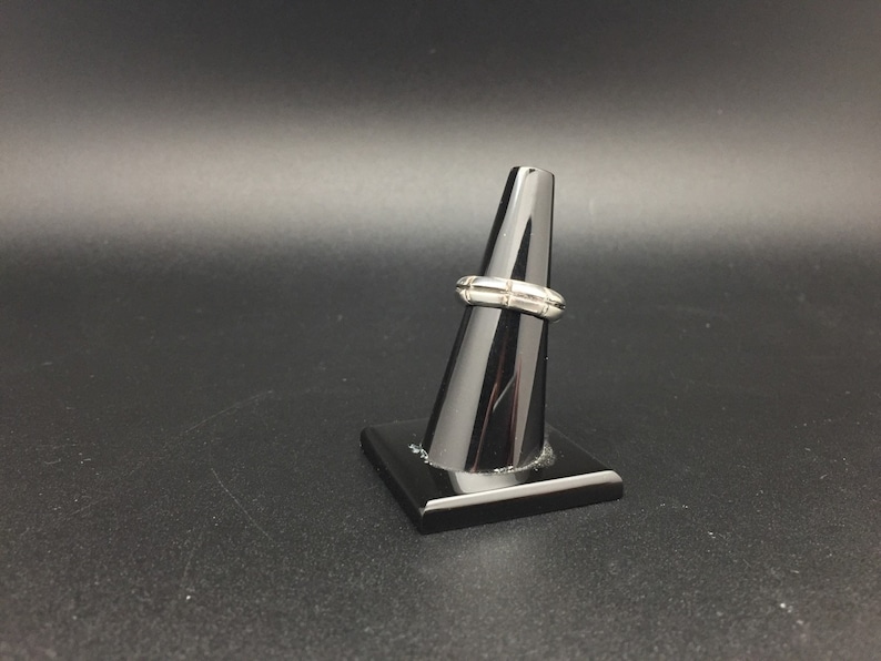 May include: A silver ring with a textured design. The ring is displayed on a black ring stand.
