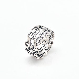 Op de afbeelding: Een zilveren ring met een delicaat, ingewikkeld ontwerp van draaiende patronen. De ring is breed en heeft een gladde, gepolijste afwerking.