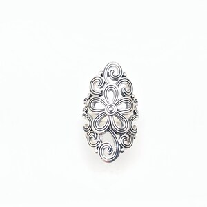 May include: A silver-colored ring with a floral design. The ring features a central flower with a circular center and petals, surrounded by swirling, openwork patterns. The ring is set against a white background.