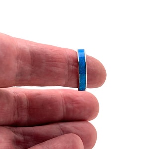 Könnte beinhalten: Ein silberner Ring mit einem Band aus blauem und türkisfarbenem Inlay. Der Ring wird vor einem weißen Hintergrund gezeigt. Der Ring ist ein einfacher Bandstil mit glatter, polierter Oberfläche.