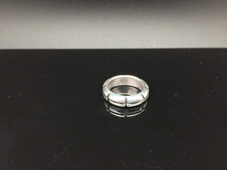 May include: A silver ring with a textured band. The band has a series of small, evenly spaced cuts around the circumference.