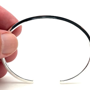 May include: A silver bangle bracelet with a smooth, rounded surface.