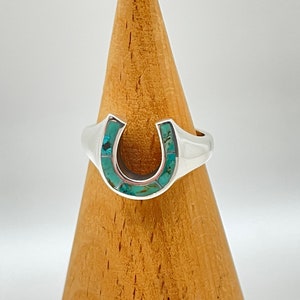 May include: A silver ring with a turquoise horseshoe design.