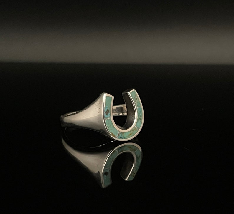 May include: A silver ring with a turquoise horseshoe design.