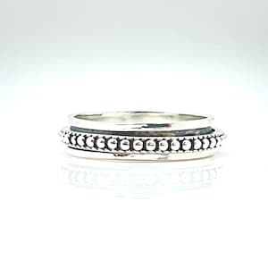 May include: A silver spinning ring with a beaded band. The ring has a textured surface and is designed to spin freely.