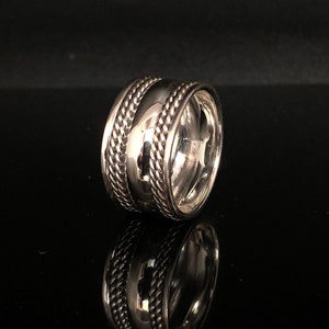 Puede incluir: Un anillo de plata con una banda ancha y un diseño trenzado. La banda es texturizada y tiene un acabado pulido.