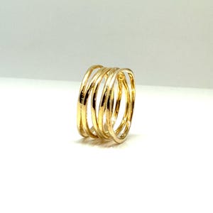 May include: A gold-colored ring with a multi-band design. The ring features five bands that are interlocked, creating a unique and modern look. The bands have a slightly textured surface, adding visual interest to the piece.