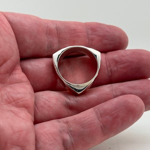 May include: A silver ring with a triangular shape. The ring is smooth and has a polished finish.
