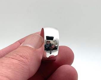 May include: A polished silver-tone band ring with a smooth, reflective surface. The metal finish is highly reflective, showing a clear mirror-like quality that captures the surrounding environment on its curved, rounded exterior surface.