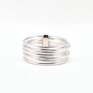 May include: A silver ring with multiple thin bands wrapped around each other. A small rectangular piece connects the bands. The ring is on a white background. The ring is a piece of jewelry.