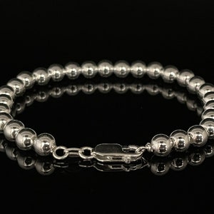 May include: A silver beaded bracelet with a lobster clasp fastening. The bracelet is made of round beads and has a polished finish.
