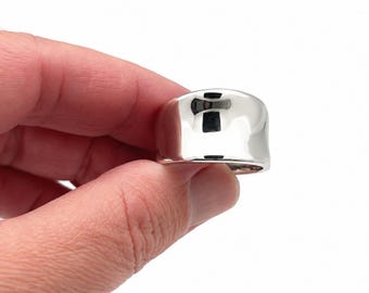 Può includere: Un anello largo in argento lucido con una superficie liscia e riflettente, caratterizzato da una forma organica leggermente irregolare. La fascia presenta una finitura molto brillante che cattura la luce, creando un aspetto metallico luminoso.