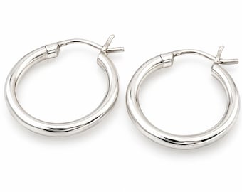 May include: A pair of polished silver hoop earrings with a smooth, rounded tubular design. Each earring features a secure hinged post closure mechanism at the top, providing a clean and continuous circular silhouette for these classic jewelry pieces.