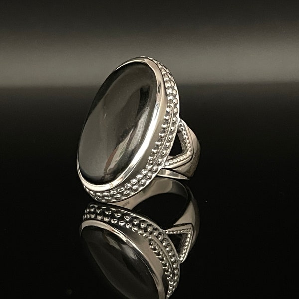 May include: A silver ring with a black oval gemstone set in a beaded bezel. The ring has a decorative band with a cutout design.