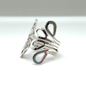 May include: A silver-colored ring with an open, flowing design. The ring features a series of interconnected, teardrop-shaped cutouts that wrap around the finger. The metal has a polished, reflective surface, creating a modern and elegant look. The ring is a piece of jewelry.