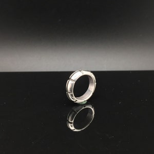 May include: A silver ring with a textured, geometric design. The ring is made of a smooth, polished metal and has a simple, modern style.