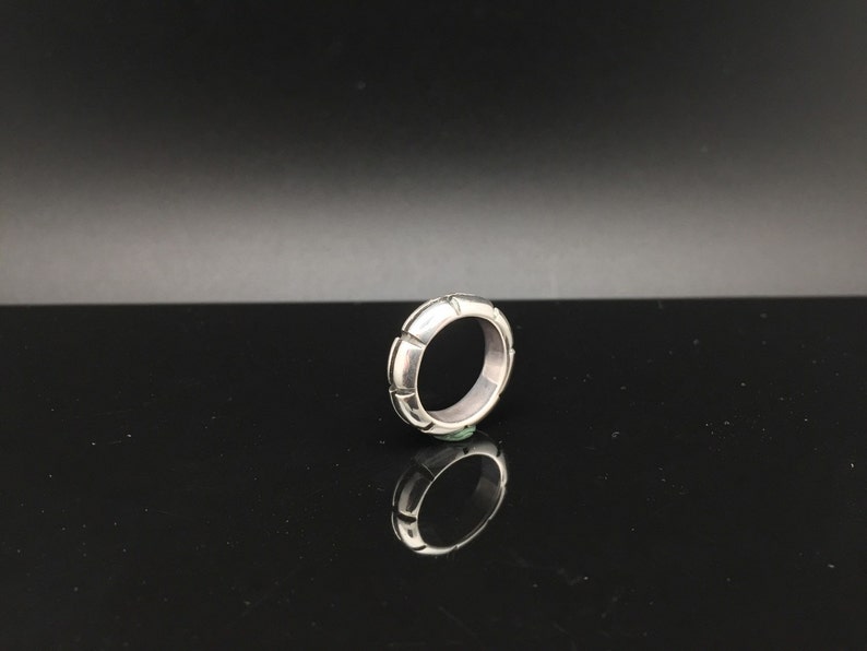 May include: A silver ring with a textured, geometric design. The ring is made of a smooth, polished metal and has a simple, modern style.