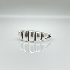 May include: A silver ring with a unique design featuring five rounded, connected segments. The ring has a smooth, polished finish.