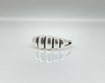 May include: A silver ring with a unique design featuring five rounded, connected segments. The ring has a smooth, polished finish.