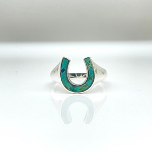 May include: A silver ring with a turquoise horseshoe design.