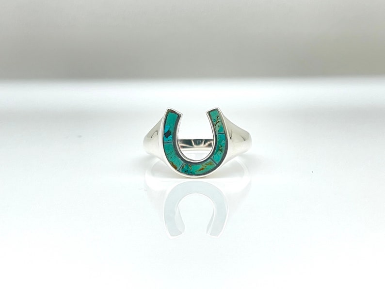 May include: A silver ring with a turquoise horseshoe design.