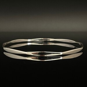 May include: A silver bangle bracelet with a smooth, slightly curved surface.