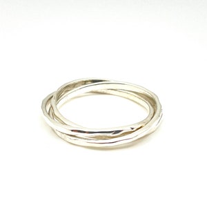 Peut inclure: Une bague en argent composée de trois anneaux entrelacés. Les anneaux sont lisses et ont une texture légèrement martelée.
