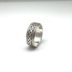 May include: A silver ring with an intricate Celtic knot design. The ring features a band of interwoven patterns around the circumference. The metal has a polished finish, reflecting light. The ring is displayed on a white background.