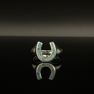 May include: A silver ring with a turquoise horseshoe design.