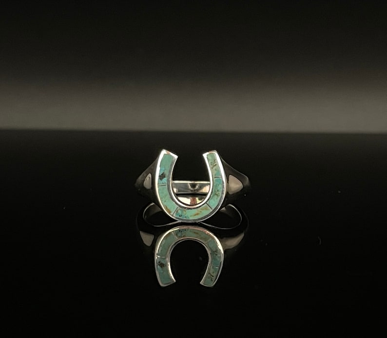 May include: A silver ring with a turquoise horseshoe design.