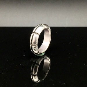 May include: A silver ring with a textured, ridged design. The ring is shown on a black background.