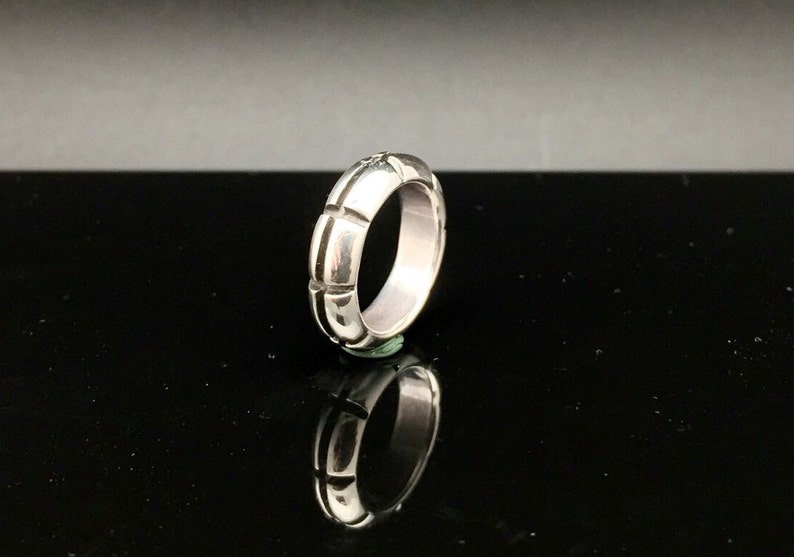 May include: A silver ring with a textured, ridged design. The ring is shown on a black background.