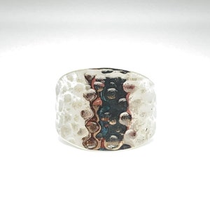 May include: A silver ring with a textured hammered finish. The ring has a wide band with a raised pattern of small circles.