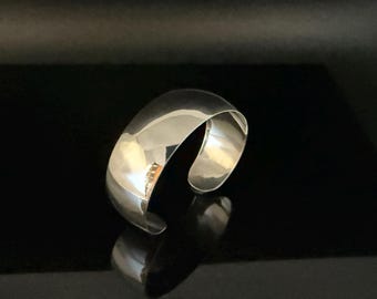 以下が含まれることがあります： 曲線的で開いたデザインの、磨かれたシルバーのカフブレスレット。ブレスレットは光を反射し、ハイライトと影を作り出します。ジュエリーは黒い表面に展示されており、その輝きを増しています。このアクセサリーは日常使いに適しています。