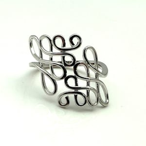 May include: A silver-toned ring featuring an openwork design composed of multiple interconnected, swirling wire loops. The metal surface is polished and reflective, creating a continuous, flowing pattern that wraps around the finger band.