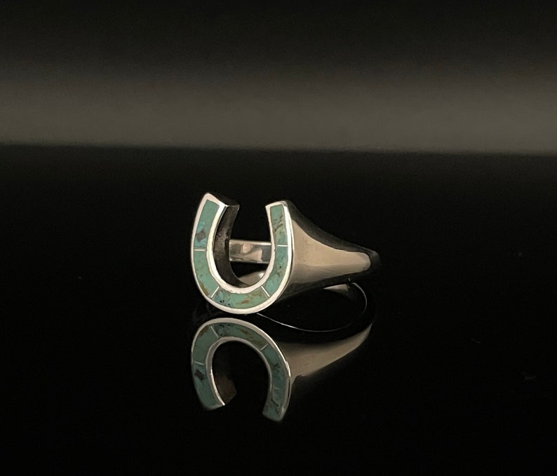 May include: A silver ring with a turquoise horseshoe design.