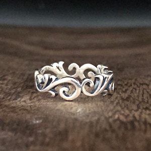 Puede incluir: Un anillo de plata con un delicado y complejo diseño de espirales y curvas.