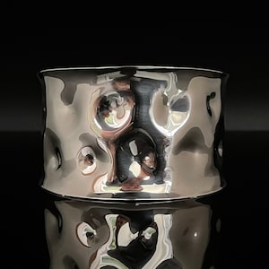 Può includere: Un braccialetto rigido in metallo argentato martellato con una superficie testurizzata.