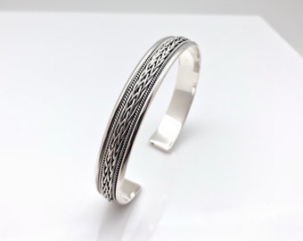 May include: A silver bangle bracelet with a braided design.
