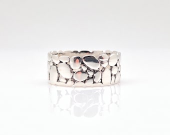 Puede incluir: Un anillo de plata con un diseño texturizado que se asemeja a un grupo de pequeñas piedras.