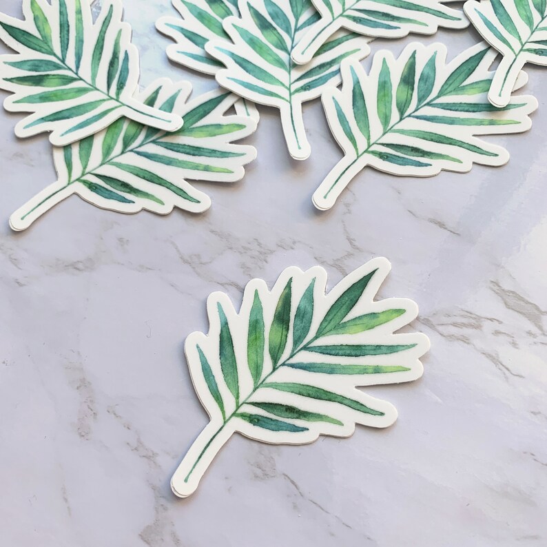 May include: A set of green watercolour palm leaf stickers. The stickers are on a white marble background.